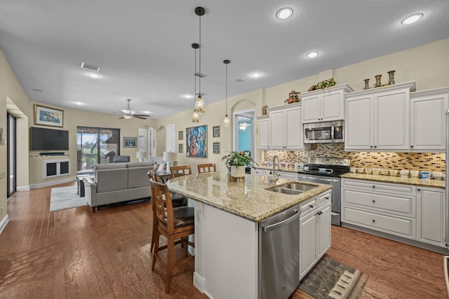 kitchen with appliances with stainless steel finishes, dark hardwood / wood-style flooring, white cabinetry, and an island with sink