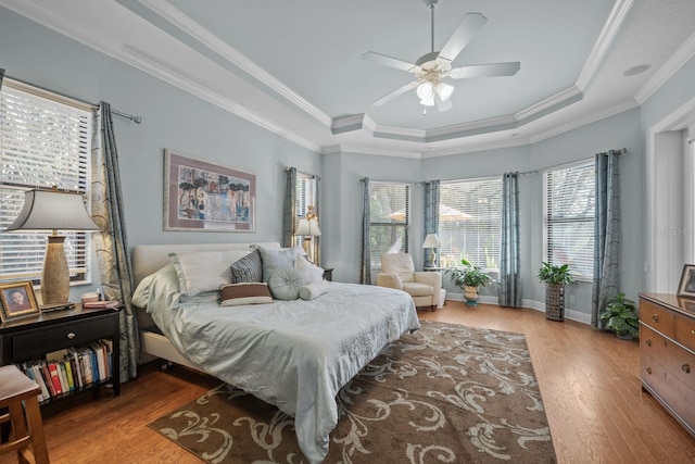 bedroom featuring hardwood / wood-style floors, ceiling fan, crown molding, and a tray ceiling