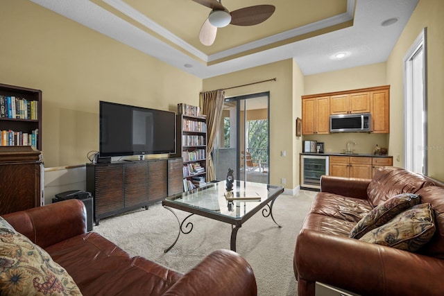 living room featuring light carpet, crown molding, wine cooler, ceiling fan, and a tray ceiling