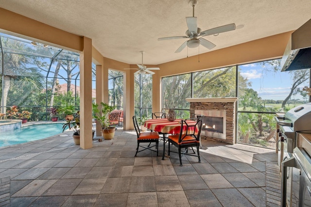 sunroom featuring an outdoor stone fireplace, ceiling fan, a pool, and a wealth of natural light