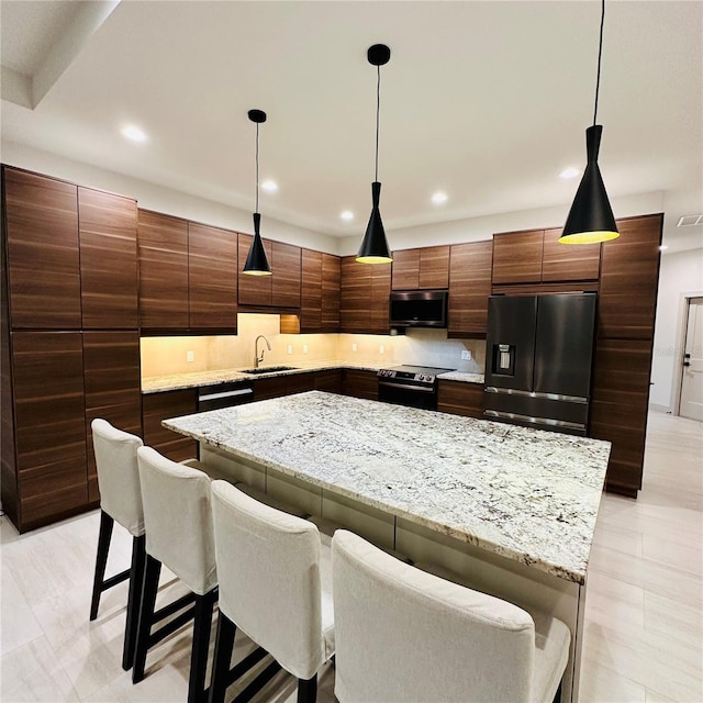 kitchen with a kitchen breakfast bar, sink, a center island, decorative light fixtures, and appliances with stainless steel finishes