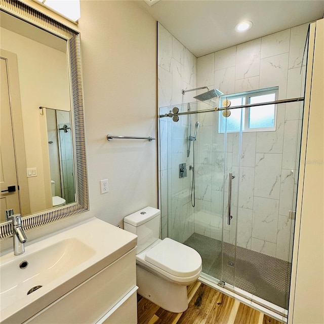 bathroom with toilet, a shower with shower door, hardwood / wood-style flooring, and vanity