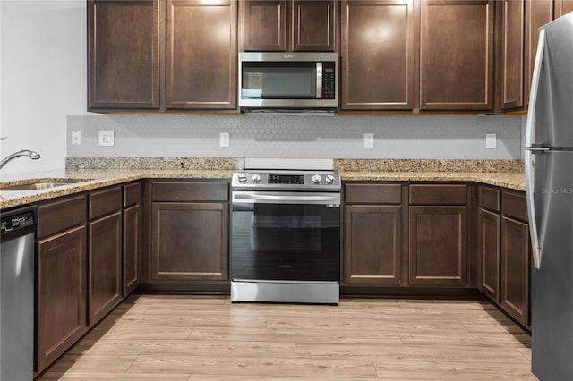 kitchen featuring appliances with stainless steel finishes, sink, dark brown cabinetry, light stone counters, and light hardwood / wood-style flooring