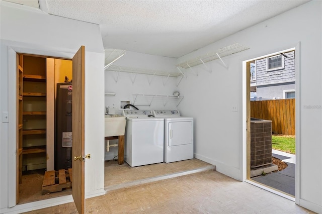 laundry area featuring washing machine and clothes dryer, water heater, sink, and a textured ceiling