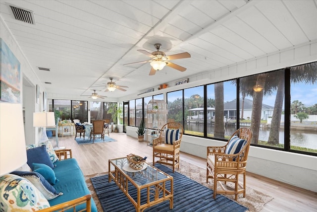 sunroom with ceiling fan and a water view