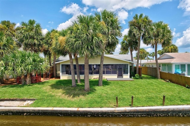 back of property featuring a sunroom, a water view, and a lawn