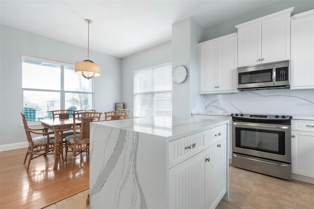 kitchen featuring appliances with stainless steel finishes, white cabinetry, light stone countertops, light hardwood / wood-style flooring, and decorative light fixtures