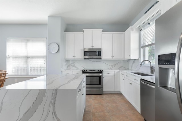 kitchen featuring backsplash, appliances with stainless steel finishes, white cabinetry, light stone countertops, and sink