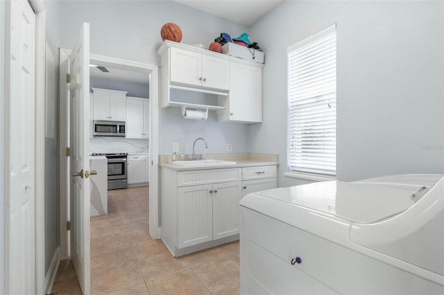 kitchen with sink, appliances with stainless steel finishes, white cabinetry, and light tile patterned flooring