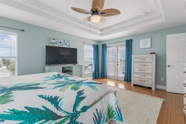 bedroom with a tray ceiling, access to exterior, light wood-type flooring, and ceiling fan