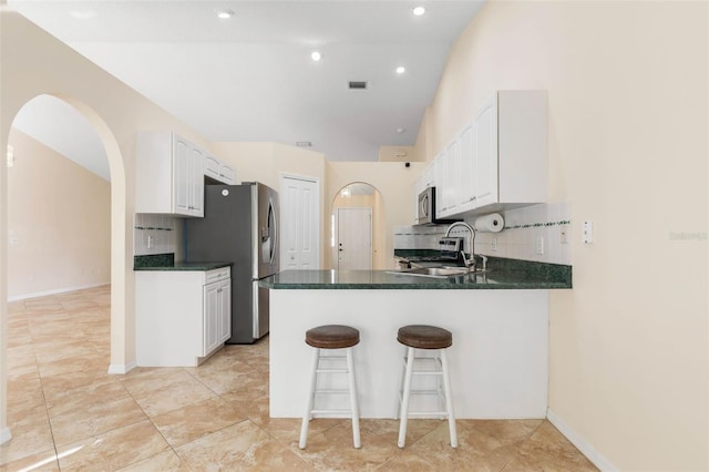 kitchen featuring kitchen peninsula, backsplash, appliances with stainless steel finishes, a breakfast bar, and white cabinetry