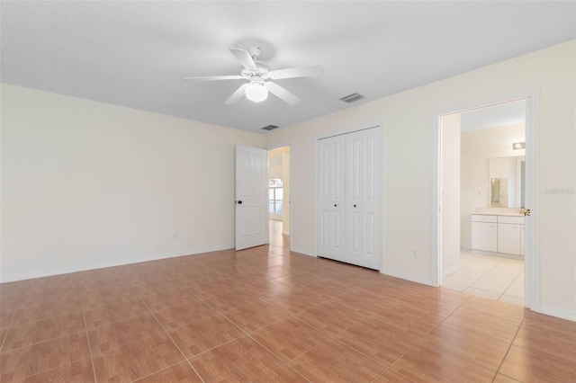 unfurnished bedroom with ensuite bath, light tile patterned floors, and ceiling fan