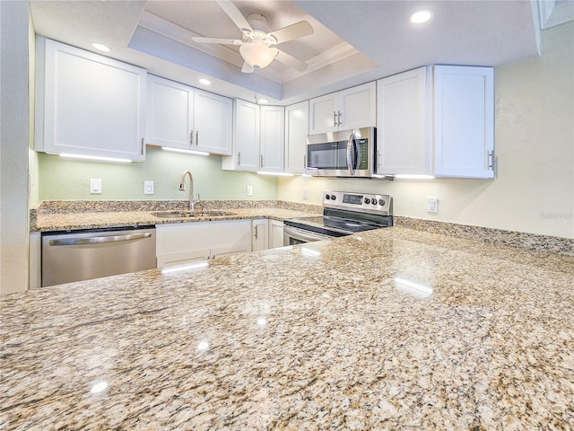 kitchen featuring sink, light stone countertops, white cabinetry, a raised ceiling, and appliances with stainless steel finishes