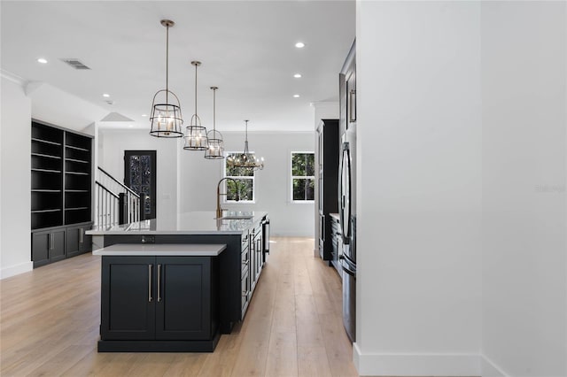 kitchen featuring crown molding, light hardwood / wood-style floors, hanging light fixtures, sink, and an island with sink