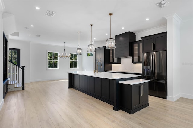 kitchen featuring hanging light fixtures, a large island, stainless steel fridge with ice dispenser, wall chimney range hood, and an inviting chandelier