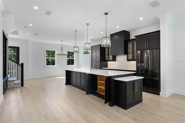 kitchen with light hardwood / wood-style flooring, hanging light fixtures, stainless steel fridge with ice dispenser, wall chimney range hood, and a large island with sink