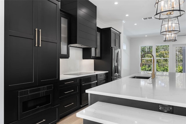 kitchen with decorative light fixtures, sink, wall chimney range hood, and a kitchen island with sink