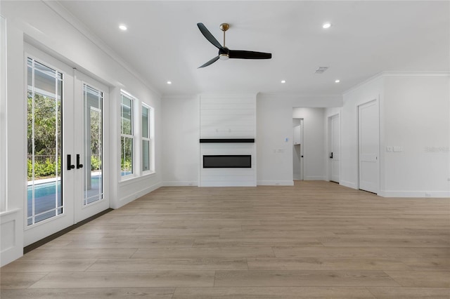 unfurnished living room featuring french doors, light hardwood / wood-style floors, a large fireplace, ceiling fan, and crown molding