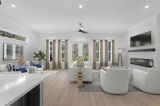 living room featuring ceiling fan, french doors, a fireplace, ornamental molding, and light hardwood / wood-style floors