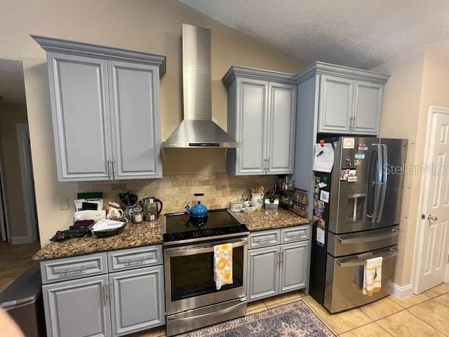 kitchen featuring light tile patterned flooring, wall chimney range hood, stainless steel appliances, and dark stone countertops