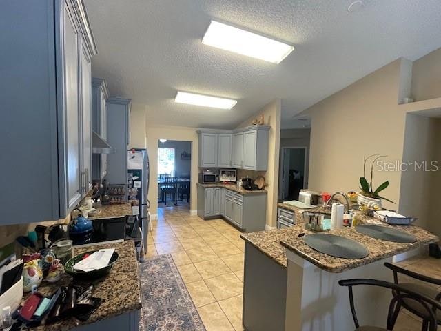 kitchen with light tile patterned flooring, a textured ceiling, kitchen peninsula, dark stone countertops, and a breakfast bar area