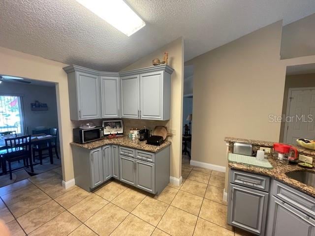 kitchen with lofted ceiling, light tile patterned floors, a textured ceiling, dark stone counters, and gray cabinetry