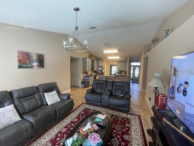 living room featuring light tile patterned flooring, lofted ceiling, a textured ceiling, and a chandelier