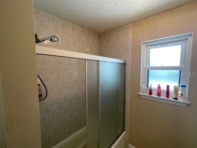 bathroom with bath / shower combo with glass door and a textured ceiling