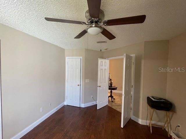 unfurnished bedroom featuring a textured ceiling, dark wood-type flooring, and ceiling fan