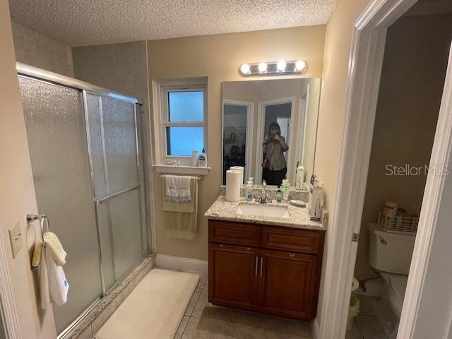 bathroom featuring vanity, a textured ceiling, toilet, and walk in shower