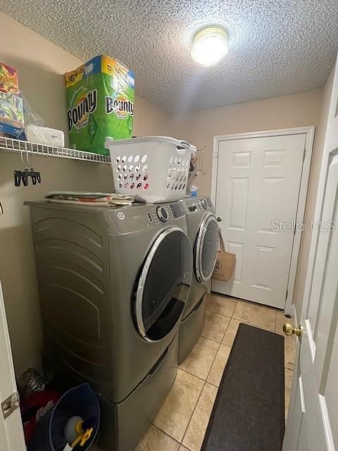 washroom with a textured ceiling, washer and clothes dryer, and light tile patterned floors