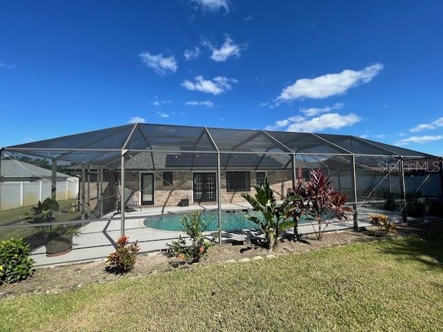 view of swimming pool featuring a patio area, a yard, and glass enclosure