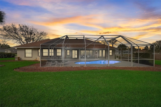 back house at dusk featuring a yard, a patio area, and glass enclosure