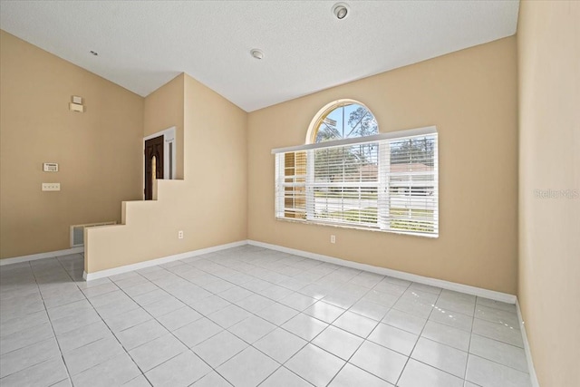 tiled empty room with lofted ceiling and a textured ceiling