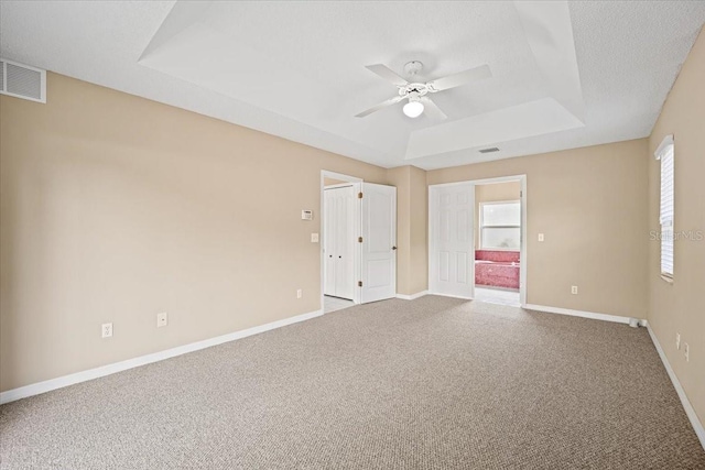 empty room with a textured ceiling, ceiling fan, carpet floors, and a raised ceiling