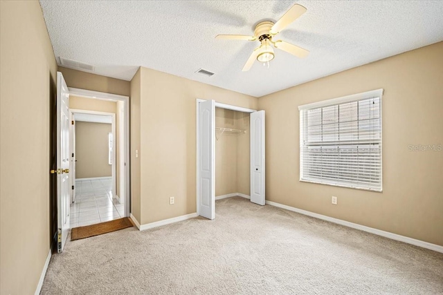 unfurnished bedroom with a textured ceiling, light colored carpet, a closet, and ceiling fan