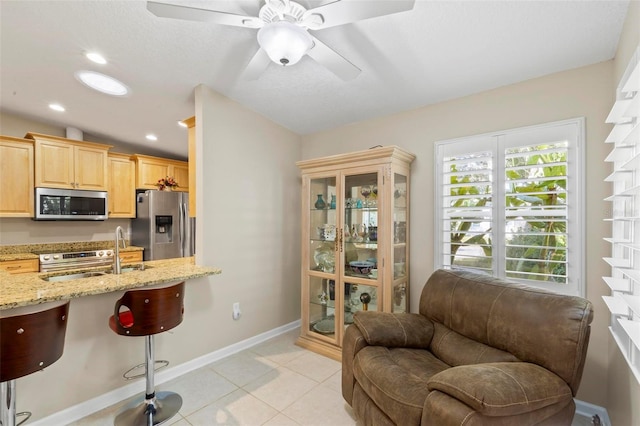 kitchen featuring light brown cabinetry, light stone countertops, a kitchen bar, stainless steel appliances, and light tile patterned floors