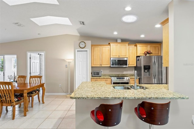 kitchen featuring kitchen peninsula, appliances with stainless steel finishes, light stone countertops, lofted ceiling with skylight, and sink