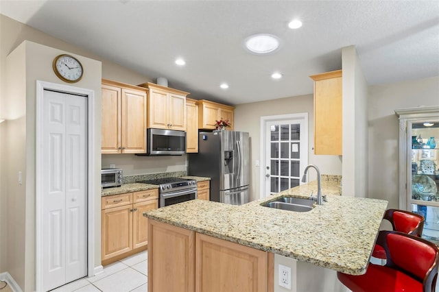 kitchen with kitchen peninsula, stainless steel appliances, sink, a breakfast bar, and light brown cabinetry