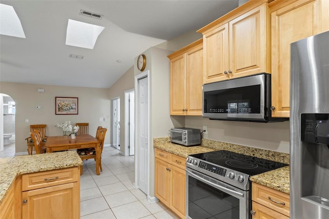 kitchen with light tile patterned floors, appliances with stainless steel finishes, light brown cabinetry, lofted ceiling with skylight, and light stone counters