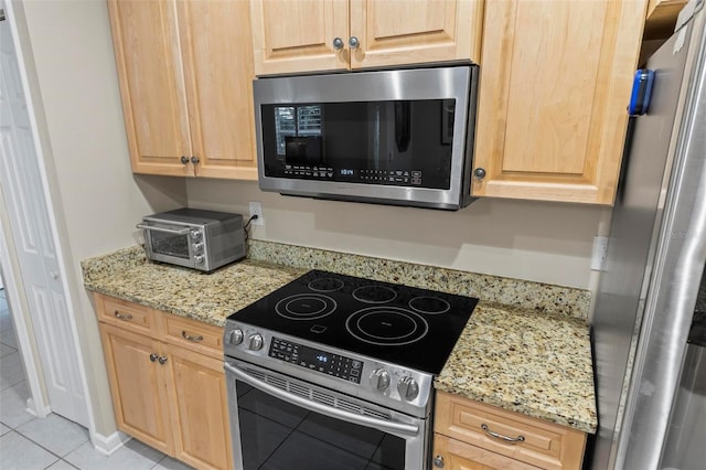 kitchen with appliances with stainless steel finishes, light stone counters, and light tile patterned floors