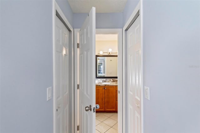 corridor with light tile patterned floors, a textured ceiling, and sink