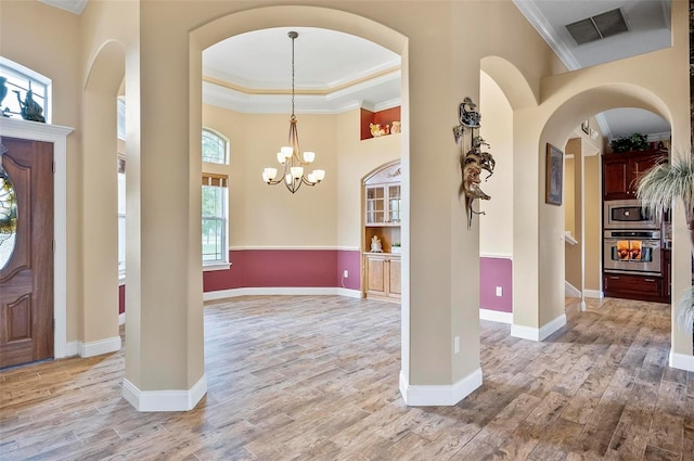 entryway featuring a notable chandelier, ornamental molding, a tray ceiling, and light wood-type flooring