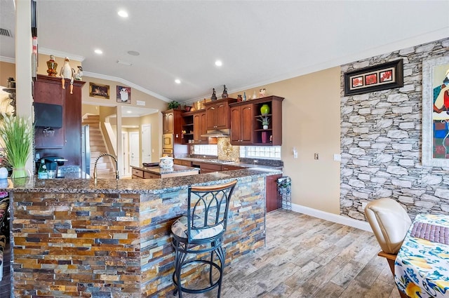 kitchen with lofted ceiling, kitchen peninsula, stainless steel appliances, crown molding, and light wood-type flooring