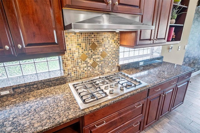 kitchen with light hardwood / wood-style flooring, stainless steel gas stovetop, dark stone counters, and backsplash