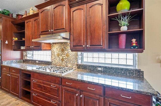 kitchen featuring decorative backsplash, stainless steel gas stovetop, a textured ceiling, dark stone countertops, and light hardwood / wood-style floors