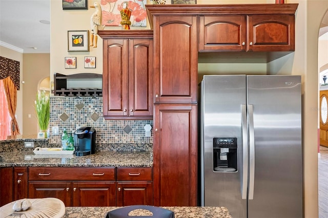 kitchen featuring dark stone countertops, decorative backsplash, ornamental molding, and stainless steel fridge