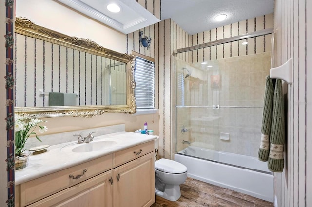 full bathroom featuring a textured ceiling, wood-type flooring, shower / bath combination with glass door, toilet, and vanity