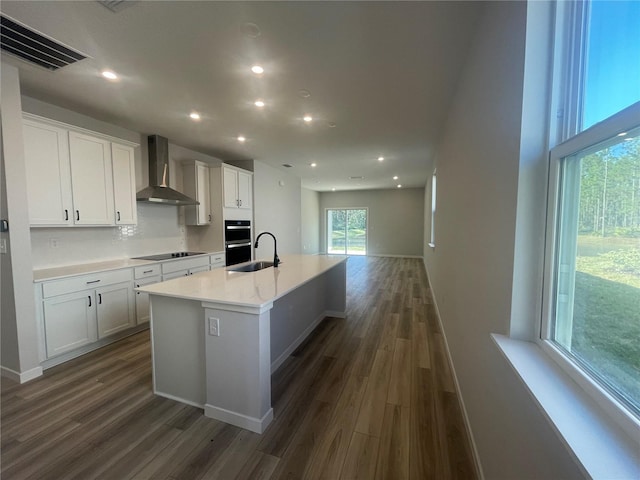 kitchen with a kitchen island with sink, wall chimney range hood, dark hardwood / wood-style floors, and white cabinets