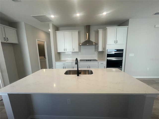 kitchen with white cabinetry, sink, an island with sink, and wall chimney exhaust hood